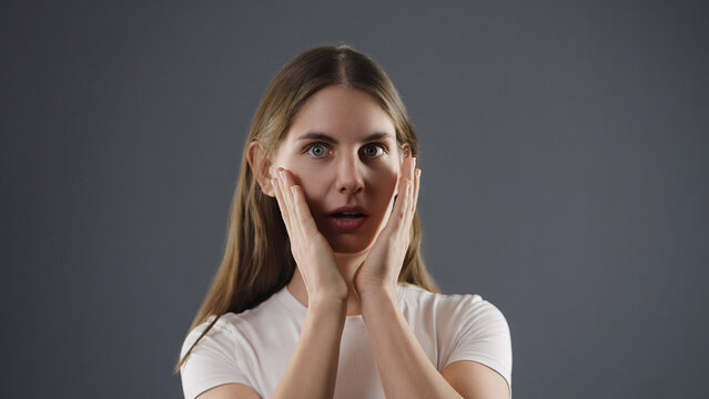Young woman showing an expression of shock and fear with hands touching cheeks