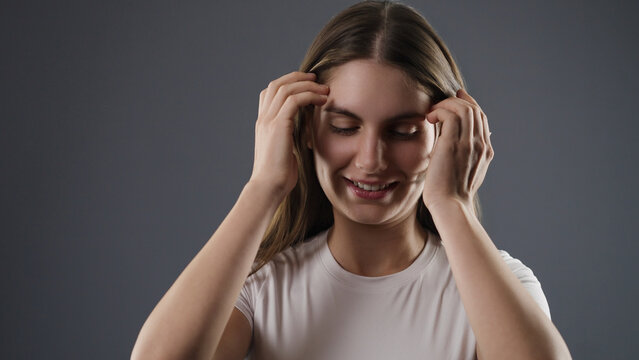 Young woman with closed eyes smiling, touching her hair, feeling happiness and self care