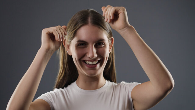 Young woman in white t shirt laughing and raising hands on a gray background
