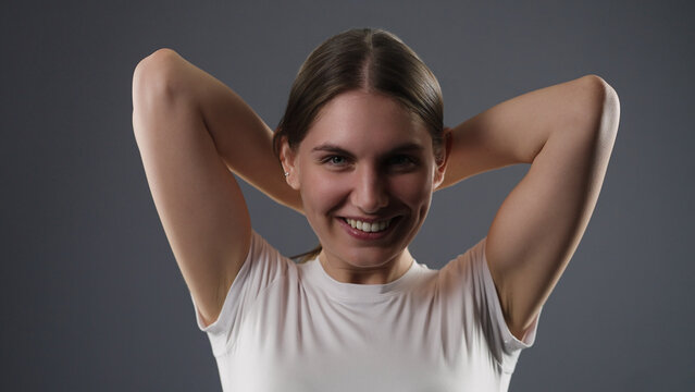 Young woman with brown hair smiling at camera with arms clasped behind head