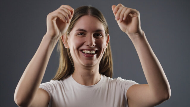 Young woman smiling with joy, expressing happiness and excitement against a grey background