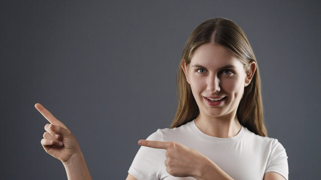 Young woman pointing fingers to the left and up, presenting a concept with copy space