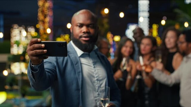Close up of a man using a smartphone front camera to take group selfies as jolly partygoers pose together at a nighttime social gathering.