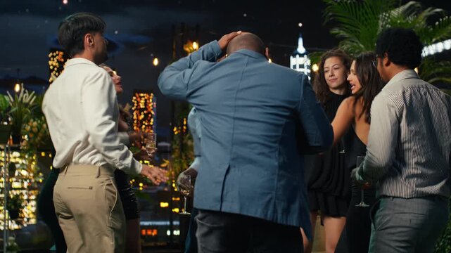 Ecstatic men and women cheer and dance at a rooftop party as thrilled partygoers sing to music and raise champagne flutes during the celebration.
