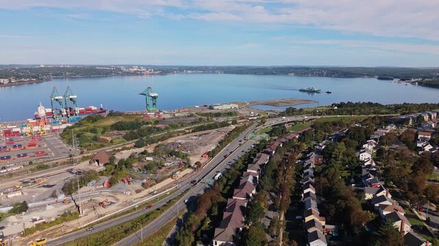 Aerial cinematic shot of a military ship towing another vessel across Halifax Harbour at sunrise, passing under a bridge with the city skyline and waterfront visible beyond.