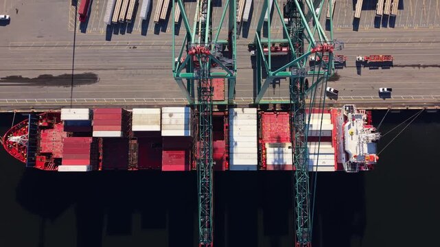Aerial drone shot of a large container vessel alongside the Halifax waterfront terminal, with heavy cranes transferring intermodal containers from the ship to trucks for inland transportation.