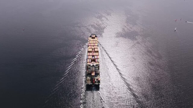 Cinematic aerial shot of a large container ship departing the Port of Halifax, Nova Scotia, Canada, with colorful intermodal containers packed across the vessel as it sails toward open Atlantic waters