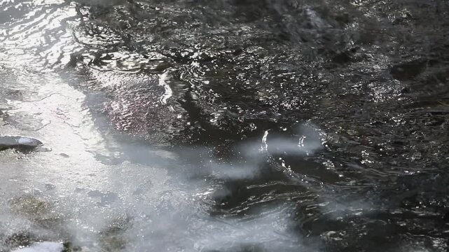 Water flowing over an ice surface with light reflections on the water surface, Mondseeland, Salzkammergut, Austria