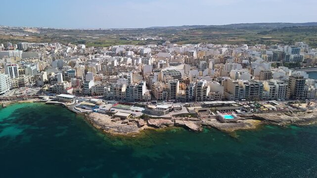 St Paul's Bay and Bugibba, Malta seafront with coastal cityscape, hotels, apartments and promenade along the Mediterranean Sea on a sunny day, aerial view.