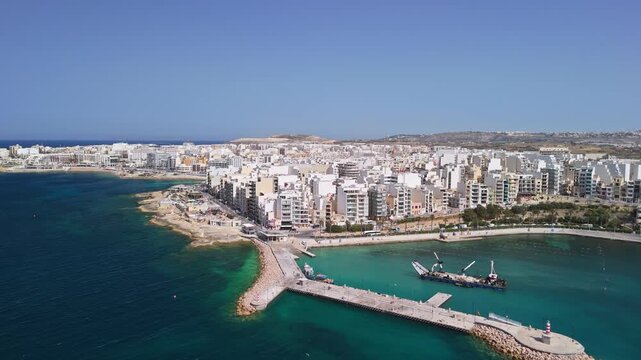 St Paul's Bay, Malta harbor with dredging vessel near Bugibba breakwater construction, clear Mediterranean waters and coastal cityscape viewed by drone on a sunny spring day.