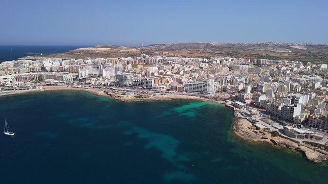 St Paul's Bay and Bugibba, Malta waterfront with hotels, residential buildings and boats along the rocky Mediterranean coast on a sunny spring day, captured by drone.