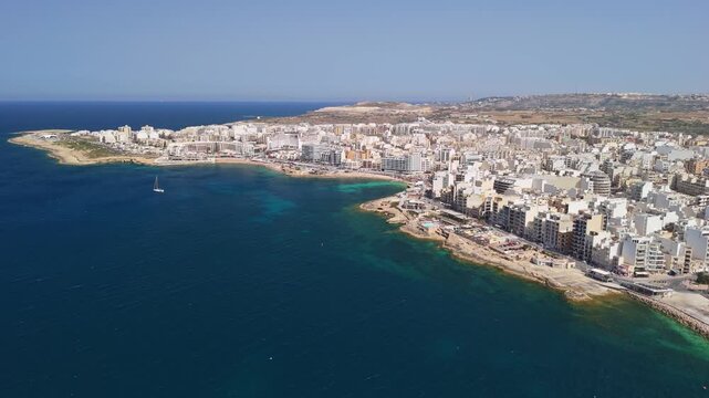St Paul's Bay in Malta with Bugibba and Qawra waterfront skyline, marina and apartment buildings along the Mediterranean coast on a sunny spring day, captured by drone.