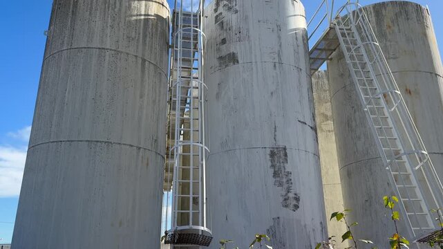 A tilt up over a dilapidated petroleum bulk plant, showcasing rusted tanks and weathered structures under a clear blue sky.