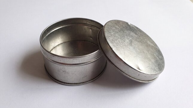 Empty round metal tin container with open lid resting sideways on white background