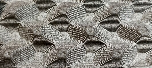 Close‑up of a precision‑machined metallic surface featuring concentric hexagonal and diamond‑like grooves.The repeating geometric pattern creates a striking three‑dimensional effect with raised center © Johari