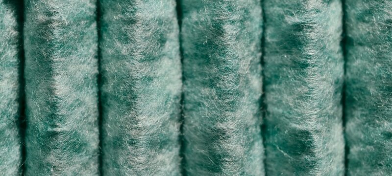 Macro view of parallel cylindrical shapes covered in dense fibrous material with muted greenish-blue tones. The plush, fuzzy surface creates a soft, textured appearance, suitable for fabric theme. 