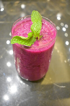 Fresh red dragon fruit smoothie topped with green mint leaves served in a glass