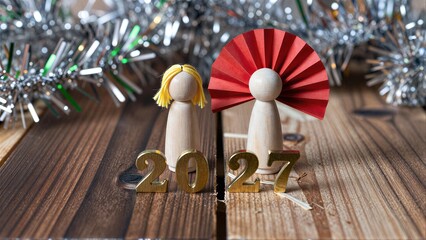Fototapeta premium Wooden angels with red wings stand beside 2027 on a rustic wooden table.