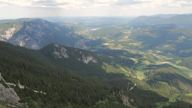 A valley with mountains and trees shows changing light and shadows throughout the day.
