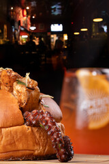 Shrimp and octopus sandwich on a wooden board, with a spritz cocktail in the blurred background. © mario