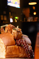 Octopus tentacle on a shrimp and octopus seafood sandwich, served on a wooden board with a spritz cocktail in the blurred background. © mario