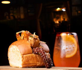 Shrimp and octopus sandwich on a wooden board, with a spritz cocktail in the background. © mario