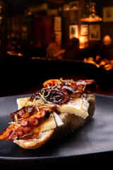 Close-up of a seafood bruschetta with octopus tentacle and Brie cheese, with a blurred restaurant background. © mario