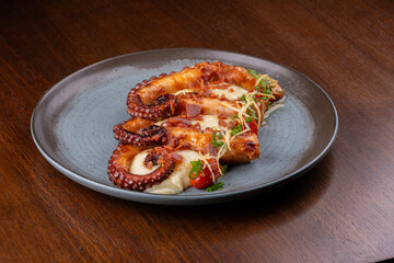 Gourmet dish of three cooked octopus tentacles served with mashed potatoes on a wooden table. © mario
