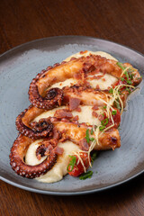 Close-up of a gourmet dish featuring three tentacles of cooked octopus served with vegetable-infused mashed potatoes on a wooden table. © mario