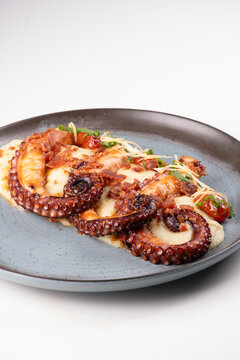 Close-up of a succulent gourmet dish featuring three tentacles of cooked octopus served with vegetable-infused mashed potatoes against a white background.