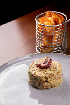 Seafood tartare dish garnished with an octopus tentacle, served with potato chips.