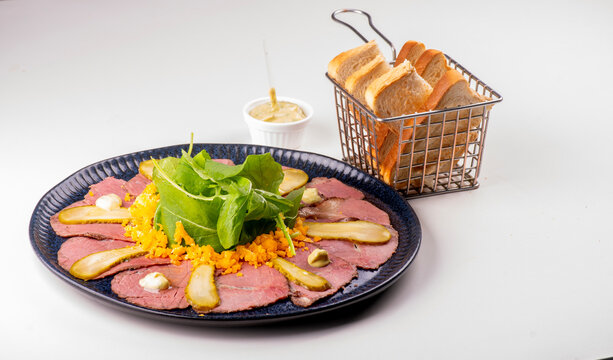 Pastrami and roast beef appetizer with arugula and toasted bread, on a white background.