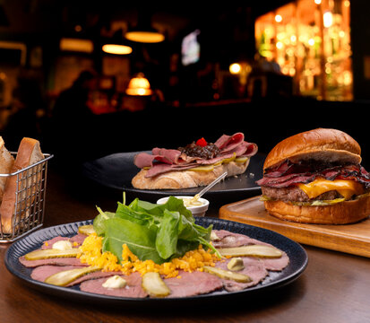 Pastrami festival featuring a cold cut platter, hamburger, and pastrami and roast beef bruschetta at a pub-style restaurant.