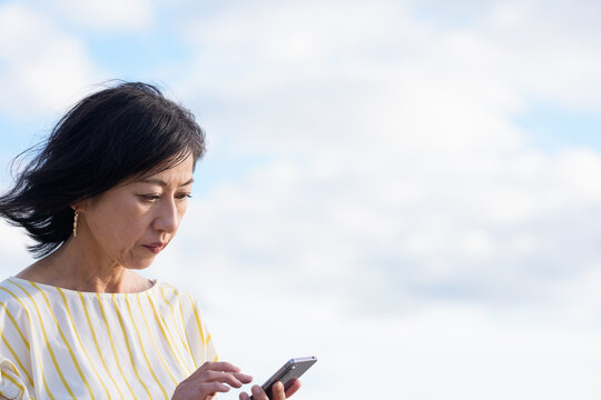 不安そうに携帯電話を動作するシニア女性