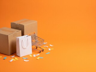 Cardboard boxes, white shopping bag and mini cart on orange background © Enjun