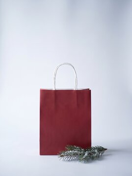 Burgundy paper shopping bag with white handles and snowy pine branch