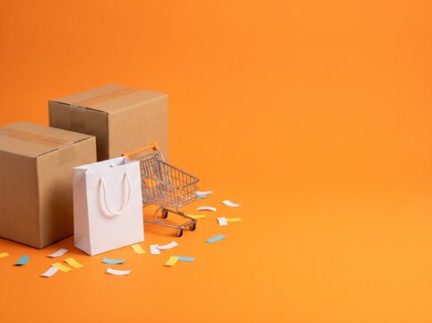 Cardboard boxes, white shopping bag and mini cart on orange background