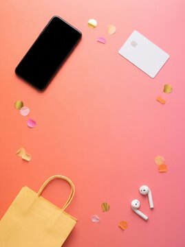 Smartphone, blank card, earbuds and paper bag on coral background