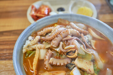 Nakji jjamppong, spicy Korean seafood soup with whole octopus tentacles, mussels, and vegetables in red chili broth, served in a stone bowl with kimchi side dishes. © 진영김