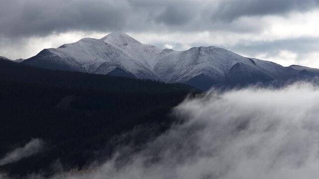 Aerial of snow capped mountain peaks and thick fog rolling through the forested valleys of the Sawatch Mountain Range in Gunnison National Forest near Sargents Colorado in fall