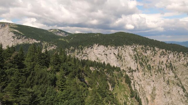 Clouds move over a mountain range, revealing rocky cliffs and green forests below.
