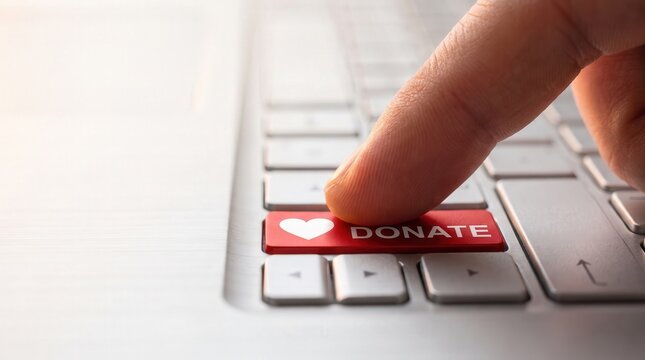 Human finger pressing red donate button with heart icon on laptop keyboard, capturing the concept of digital philanthropy and online giving for non-profit fundraising and charity marketing.