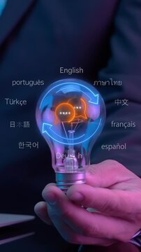 Hand holding glowing lightbulb vertical shot surrounded by multilingual language floating words. International communication innovation, cultural language education knowledge, and creative concept.