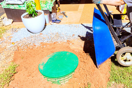 Worker is working in yard with green septic tank lid on ground wheelbarrow is nearby.