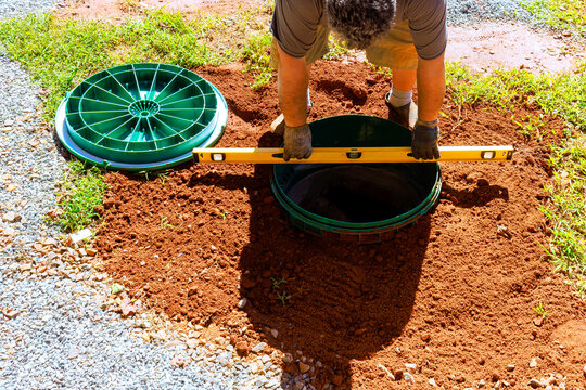 Worker works in yard placing septic tank cover using level to ensure proper positioning.