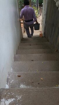 Young Man Carrying Bucket with Chili Pepper Plant Down Stairs