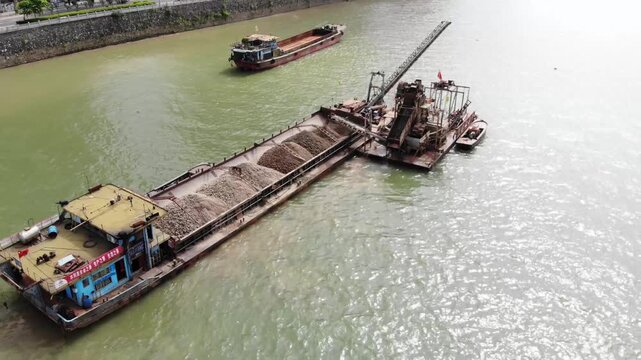 Aerial view of cargo barges and dredging vessel transporting sand on a city river