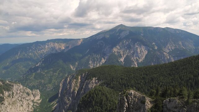 Clouds drift over peaks while light shifts across the rocky landscape and trees.