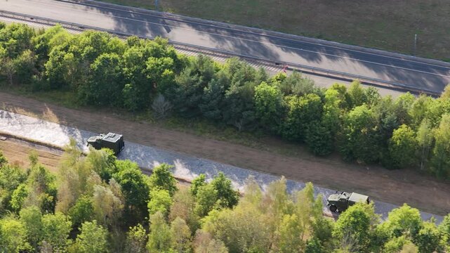 Green tactical military vehicle drives along a narrow concrete track surrounded by dense green trees and foliage at a specialized vehicle testing facility during the day