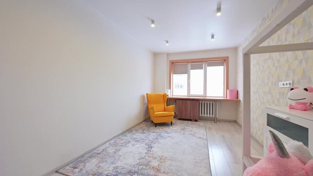 Light-toned room features yellow armchair, patterned rug, window with wooden frame, radiator, geometric-patterned wall, children&rsquo;s storage unit, pink unicorn plush toy